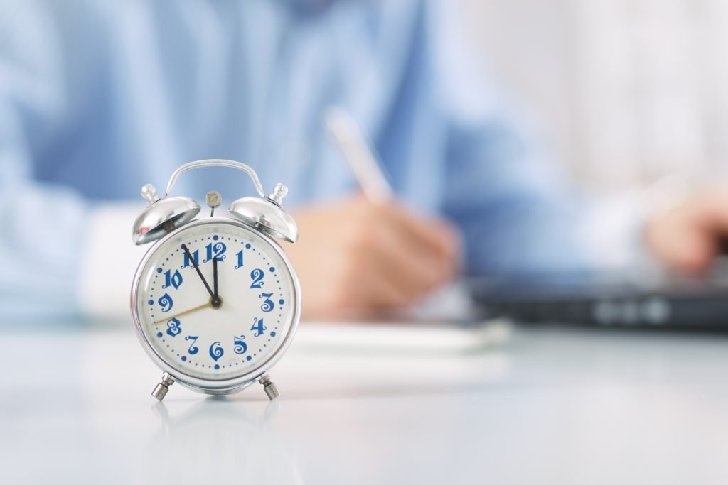 Man working in office. Clock in focus in foreground